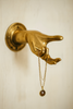 Solid brass hand wall hook holding jewelry on a light wall