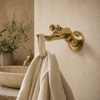 Brass fingering hand wall hook mounted on a beige wall holding a towel, funny novelty coat hook and bathroom decor.