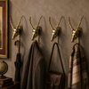 Four solid brass impala skull wall hooks mounted in a dark moody entryway with coats and bags hanging — gothic dark academia skull coat hanger set handmade in Ubud Bali