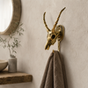 Solid brass impala skull wall hook on a neutral wall beside a round mirror with grey towel hanging — african animal skull wall hook boho home decor handmade in Bali