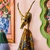 Solid brass impala skull wall hook mounted on a colorful eclectic pink wall beside floral artwork with patterned scarf hanging — african animal wall hook gothic decor handmade in Ubud Bali