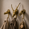 Three solid brass impala skull wall hooks mounted on a neutral wall with coats and bag hanging showing skull coat hanger gallery installation — gothic african wall hook set handmade in Ubud Bali
