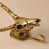 Three-quarter angled view of solid brass impala skull wall hook on a warm neutral background showing dramatic curved horn spread skull detail and hook — african gothic wall hook handmade in Ubud Bali