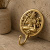 Solid brass meditating Shiva wall hook on a warm natural stone surface showing angled view of circular relief disc Lord Shiva sculpture and curved single hook — om wall hook Hindu spiritual decor ethically handmade by Balinese Hindu artisans Ubud Bali
