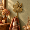 Brass maple leaf hook mounted on an olive green wall holding a plaid throw blanket, with dried flowers and candles nearby, boho home decor
