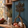 Brass maple leaf hook mounted on a blue wall shelf holding a basket of apples, with dried flowers and a window nearby