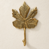 Brass maple leaf hook in a polished gold finish on a cream background