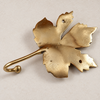 Side angle view of brass maple leaf hook in a polished gold finish showing the curved hook
