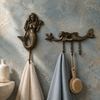 Brass mermaid wall hook with 3 connected hooks mounted on a blue wall holding a towel, boho bathroom decor.