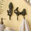 Brass mermaid wall hook set in antique finish mounted on warm yellow coastal bathroom wall beside white soap dispenser and seashell accessories. Handcrafted antique brass mermaid double hook and single hook for coastal bathroom decor, nautical home styling and beach house housewarming gift for ocean lovers