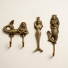 Close-up of a brass mermaid wall hook set of 3 on a cream wall, showing the double hook, arms-raised, and crowned mermaid designs.