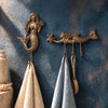 Brass mermaid wall hook set of 2 mounted on a dark blue wall holding towels, boho coastal towel and key hook set.
