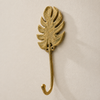Brass Monstera leaf wall hook mounted on a neutral wall, handmade boho hook with cut-leaf silhouette.
