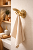 Brass mudra hand used as a bathroom robe and towel hook in a spa-style neutral bathroom.
