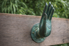 Green patina brass mudra hand wall hook mounted outdoors, shown installed on a wooden surface.