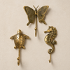 Brass ocean animal wall hook set of 3 mounted on a beige wall, showing the turtle, butterfly, and seahorse coastal coat hooks.
