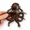 Hand holding a brass octopus wall hook in a dark aged patina finish