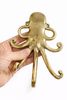 Hand holding a brass octopus wall hook in a polished gold finish