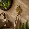 Brass palm tree wall hook polished gold finish in tropical boho bathroom holding linen towel beside round mirror stone sink and plants – palm tree towel hook coat hook – beach house coastal tropical home decor – handcrafted solid brass made in Bali UbudGlassandBrass