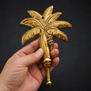 Hand holding brass palm tree wall hook against dark background showing real life size scale and polished gold hand-cast detail – banana tree brass hook – palm tree coat hook key hook towel hook – tropical boho beach house housewarming gift – solid brass handcrafted in Bali