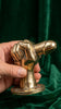 Hand holding brass penis hand wall hook at angle against deep green velvet background showing full sculptural detail mounting plate and hook – funny quirky adult after dark kinky dungeon decor – man cave bachelorette bachelor white elephant housewarming gift – polished gold Bali