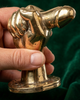 Hand holding brass penis hand wall hook close-up against rich green velvet showing real life size scale and detailed hand-cast gold texture – funny adult after dark dungeon kinky quirky decor – man cave bachelorette bachelor white elephant housewarming gift – made in Bali