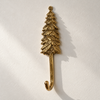 Brass pine tree hook on a plain light wall, showing the textured evergreen branches and curved hook in polished gold. A handmade Christmas tree hook and woodland gift, part of the brass deer, pine tree and maple leaf hook set of 3, from Ubud, Bali.