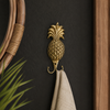 Brass pineapple double wall hook polished gold on dark background beside rattan mirror holding white towel – pineapple hook pineapple wall hook – tropical boho beach house coastal home decor – double wall hook coat hook – housewarming gift – handcrafted solid brass Bali