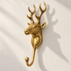 Front view of the brass reindeer wall hook on a cream wall with soft shadows, showing the detailed stag face, ears and symmetrical antlers above the curved hook. A handmade towel hook and coat hook for rustic homes, cabins and lodges, cast in Bali.