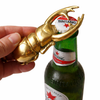 Solid brass scarab beetle bottle opener opening a beer bottle cap, handheld close-up