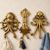 Set of three brass sea creature wall hooks — octopus, squid, and skull-octopus — mounted on a cream wall holding a cloth pouch, keys, and a striped towel