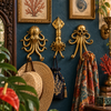 Set of three brass sea creature wall hooks — octopus, squid, and skull-octopus — mounted on a deep teal wall holding a woven hat, tasseled bag, and patterned scarf, with coastal decor and framed art nearby