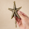 Hand holding a solid brass sea star hook to show natural size