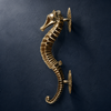 Brass seahorse door pull mounted on dark wall, antique nautical door handle