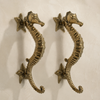 Set of two brass seahorse door pulls mounted on a cream wall, matched pair of nautical double door handles