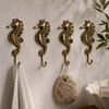 Four solid brass seahorse wall hooks mounted in a row on a neutral wall with linen towel and loofah hanging — coastal beach house bathroom hook set of 4 handmade in Ubud Bali