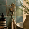 Brass seahorse wall hook mounted on a teal tiled wall near a towel, nautical coastal bathroom decor.