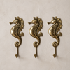 Four solid brass seahorse wall hooks displayed at an angle on a clean background showing scale detail fin texture and hook design across the complete set — coastal nautical brass hook set handmade in Bali