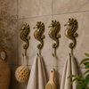 Set of 4 solid brass seahorse wall hooks mounted on stone tile bathroom wall with linen towels loofah and wooden brush hanging — coastal nautical bathroom hook set handmade in Ubud Bali