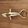 Brass seal bottle opener lying on a wooden table, seen from above with its flippers, tail and opener loop. A handmade animal bottle opener and home bar decor piece for a man cave, cast in Bali.