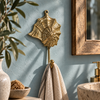 Brass seashell wall hook with spiral web design mounted on a blue wall near a wood framed mirror, holding a towel, coastal bathroom decor