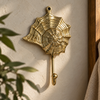 Brass seashell wall hook with spiral web design mounted on a cream wall near plants, coastal boho decor