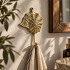 Brass seashell wall hook with spiral web design mounted near a wood framed mirror, holding a linen towel, coastal bathroom decor