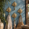 Set of four brass seashell wall hooks mounted in a row on a blue wall, holding towels, near plants and a vase, coastal nautical decor