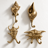 Brass seashell wall hook set of 4 on a light background, showing all four designs: a spiral conch shell hook, a Batik carved shell hook, and two spiky conch shell double hooks, one upright and one sideways. Handmade cast brass coastal towel and coat hooks, hand-finished by artisans in Ubud, Bali.