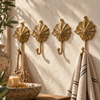 Set of four brass seashell wall hooks mounted in a row on a textured wall, holding a linen towel, near a decorative bowl, coastal bathroom decor