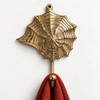 Brass seashell wall hook with spiral web design mounted on a cream wall holding a red waffle towel, nautical coastal coat hook