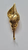 Brass carved spiral seashell hook mounted on a plain light grey wall, showing the polished gold brass finish, the Balinese scroll carving on the shell and the ball-tipped hook below. Handmade cast brass shell wall hook from Ubud, Bali.
