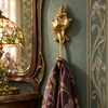 Brass shell spiral hook mounted on a dark green wall near a vintage vanity mirror holding a scarf
