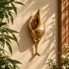 Carved brass spiral seashell wall hook mounted on a sunlit cream wall with soft palm leaf shadows and a wooden frame. Handmade cast brass shell hook with Balinese Batik-style scroll detailing and a ball-tipped hook, from Ubud, Bali.